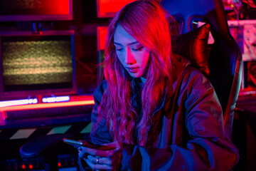 Woman hacker. Asian woman wearing hood working at computer and mobile phone typing coding hacking...