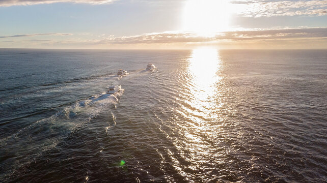 Three boats motoring towards sunrise off Gold Coast beach