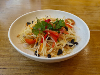 A Plate of spicy papaya salad or somtum on wooden background.