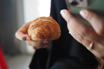 Delicious croissant held in hand while using a smartphone