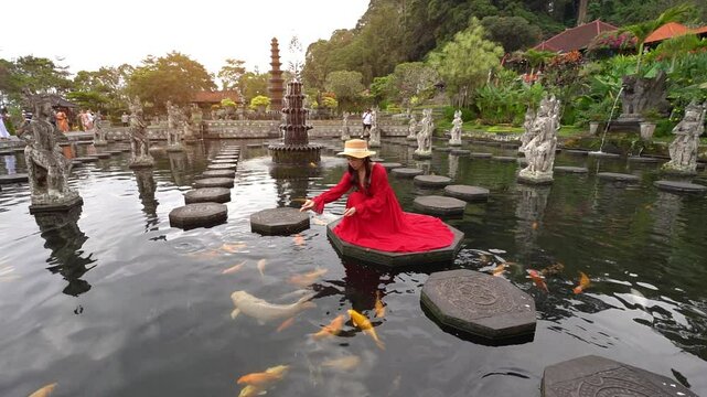 Female traveler feeds koi fish in Taman Tirtagangga Temple, Bali, Indonesia.	