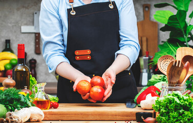 Chef holds red blood oranges in hand. Cozy kitchen with wooden table, kitchenware, vegetables, herbs and ingredients for cooking. Healthy vegan food, culinary, recipes, blogging