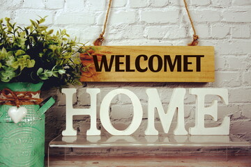 Welcome Home alphabet letters and wooden signboard hanging on white brick wall background