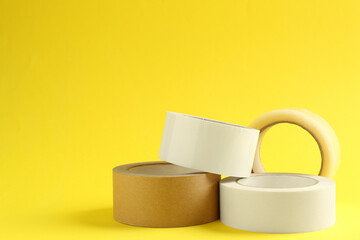Rolls of different adhesive tapes on yellow background, space for text