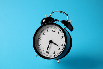Black alarm clock in air on light blue background