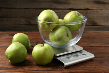 Electronic kitchen scale with bowl of green apples on wooden table, closeup