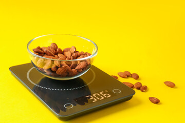 Electronic kitchen scale with bowl of almond nuts on yellow background, closeup