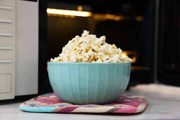 Tasty popcorn in bowl near microwave oven on light table, closeup