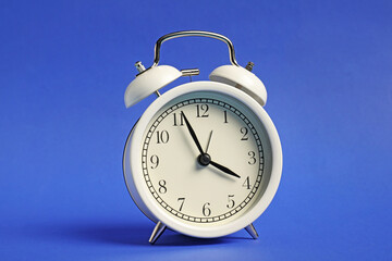 One white alarm clock on blue background