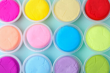 Different colorful modeling clay in plastic jars on light blue background, flat lay