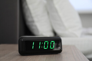 Digital alarm clock showing 11:00 o'clock on bedside table indoors