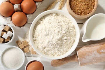 Rolling pin and ingredients for dough on white wooden table, flat lay