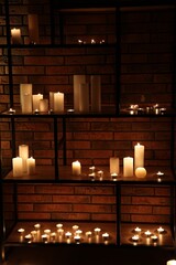 Many burning paraffin candles on shelves in dark room