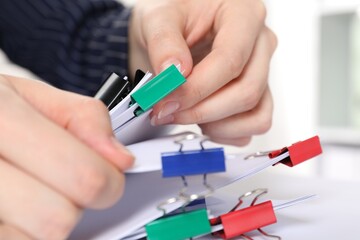 Woman attaching sheets of paper with metal binder clip indoors, closeup