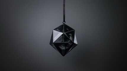A black, faceted, diamond-shaped object hangs from a black string against a dark gray background.