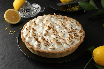 Delicious meringue pie and lemons on black textured table, closeup