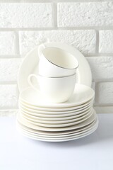 Different clean dishware on white table near brick wall