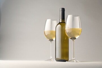 Tasty white wine in glasses and bottle on light grey background, space for text