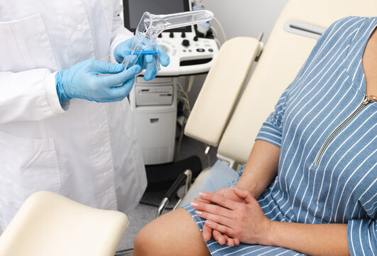 Gynecologist holding disposable vaginal speculum before examining female patient sitting on gynecological chair while routine preventative check-up