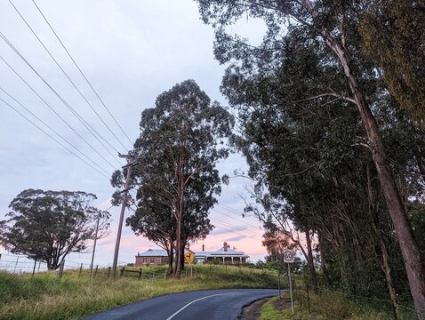Country lane at sunset lined with trees with a house in the distance in outer Sydney, Australia