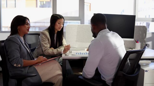 Diverse professionals collaborating during strategic financial analysis, working together at modern coworking space with data charts and shared technological resources
