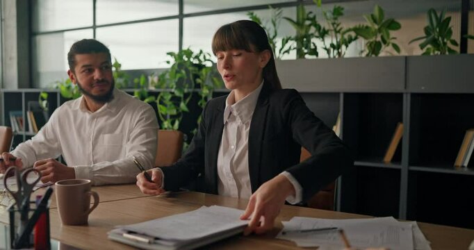 A businesswoman sits at the table sets up her laptop and tablet and joins colleagues to begin a meeting and discussion in the office