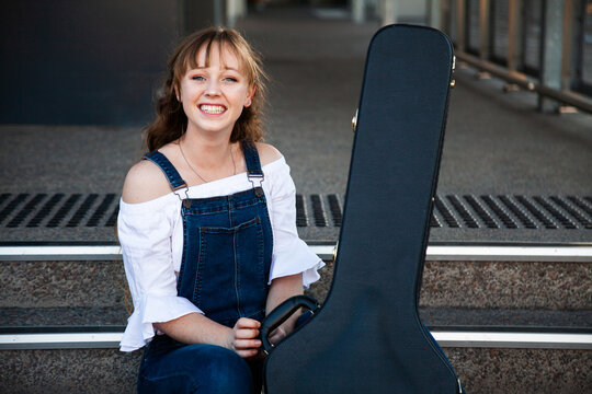 Smiling young adult with guitar case sitting on steps