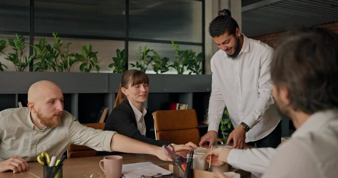 An African office worker brings lunch boxes for his colleagues placing them on the table as they gather to eat during a lunch break in the office
