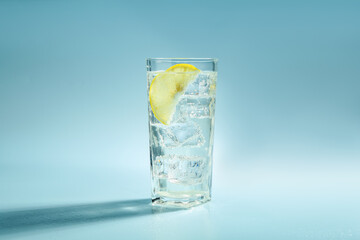Soda water with lemon and ice cubes in glass on light blue background