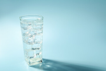 Soda water with ice cubes in glass on light blue background, space for text