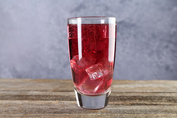 Sweet soda water with ice cubes in glass on wooden table