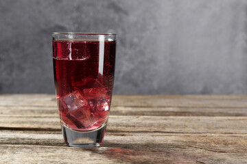 Sweet soda water with ice cubes in glass on wooden table, space for text