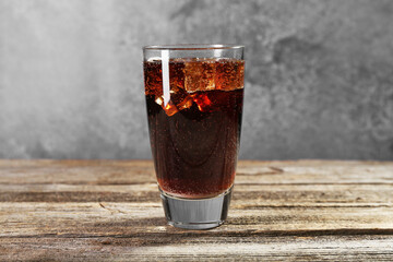 Sweet soda water with ice cubes in glass on wooden table