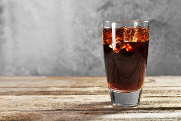 Sweet soda water with ice cubes in glass on wooden table, space for text