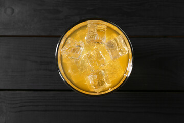 Sweet soda water with ice cubes in glass on black wooden table, top view