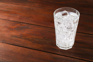 Refreshing soda water with ice cubes in glass on wooden table, space for text