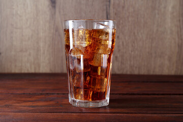 Sweet soda water with ice cubes in glass on wooden table