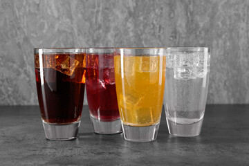 Sweet soda water of different flavors with ice cubes in glasses on grey table
