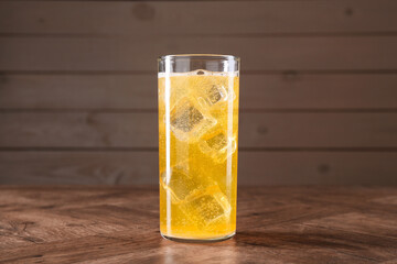 Sweet soda water with ice cubes in glass on wooden table