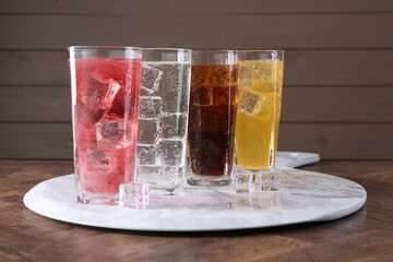 Sweet soda water of different flavors in glasses with ice cubes on wooden table