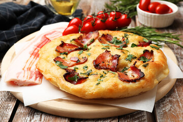 Delicious focaccia bread with bacon, parsley, tomatoes and rosemary on wooden table, closeup