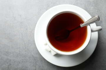 Refreshing black tea in cup and sugar cubes on grey textured table, top view. Space for text