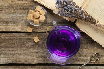 Aromatic lavender tea in cup, brown sugar, book, spoon and bunch of dry flowers on wooden table,...