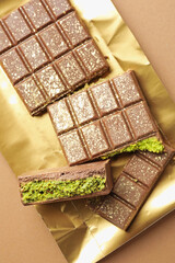 Pieces of delicious Dubai chocolate with pistachios and knafeh on dark beige background, top view