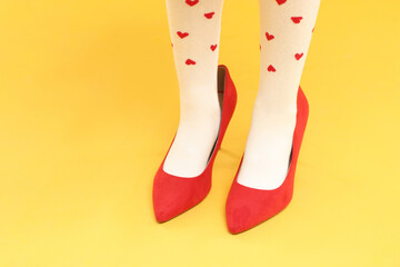 Little girl wearing oversized high heeled shoes on yellow background, closeup