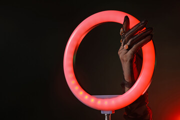 Woman wearing beautiful rings on dark red background, closeup. Using ring lamp