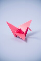 Delicate origami pink  crane on a grey background, artistic paper folding design