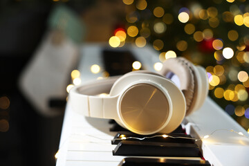 Headphones on electric piano against Christmas tree with blurred lights, closeup. Bokeh effect