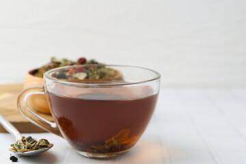 Delicious herbal tea and dry leaves on white tiled table, closeup. Space for text