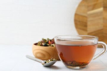 Delicious herbal tea and dry leaves on white tiled table, closeup. Space for text